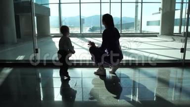 妈妈和小儿子透过机场的大窗户看飞机